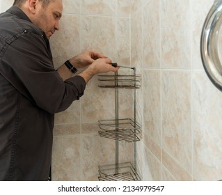 A Man In The Bathroom Unscrews The Screws With A Screwdriver Dismantling An Old Chrome Bunk Shelf Covered With Rust And Fungus