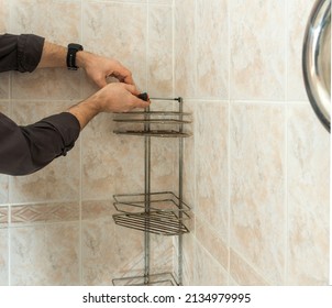 A Man In The Bathroom Unscrews The Screws With A Screwdriver Dismantling An Old Chrome Bunk Shelf Covered With Rust And Fungus