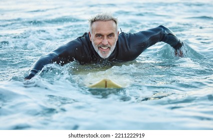 Man at beach during summer, in the ocean and surfing with surfboard for sport and fitness in a portrait. Mature, smile and surf in a wet suit for health and happy in sea water and outdoor.