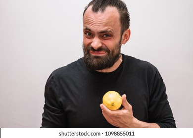 A man with a beard and a black t-shirt on a white background holds a yellow sour lemon and wrinkles