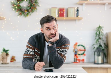 A Man With A Beard Is Bored And Is Alone At Home For Christmas, Looking At The Phone In Depression