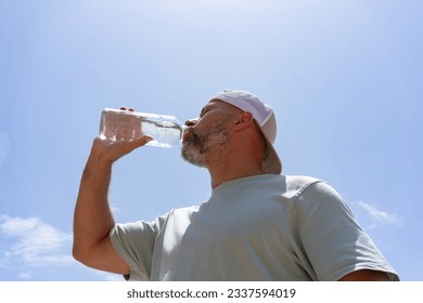 a man with a beard in a cap drinks water from a bottle on a hot 