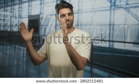 Man with beard clapping hands and smiling in airport concourse beside glass terminal windows and railing; quiet optimism.