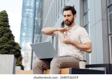 Man with beard communicating using sign language on a laptop during an online video call outdoors in an urban setting