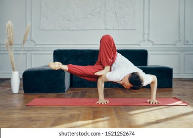 A Man With A Beard Does A Yoga Pose - A Handstand. Very Difficult Pose. A Man In A White T-shirt And Red Yoga Pants