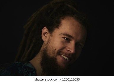 A man with a beard and dreadlocks is smiling. Man with dreadlocks over black background.