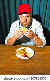 Man With Beard Eating Fast Food Meal. Enjoying French Fries And A Hamburger. Trucker With Red Cap.