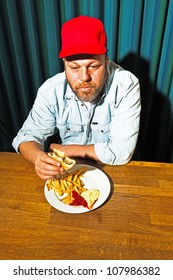 Man With Beard Eating Fast Food Meal. Enjoying French Fries And A Hamburger. Trucker With Red Cap.