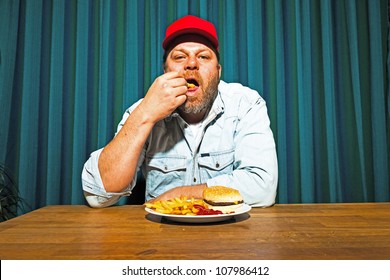 Man With Beard Eating Fast Food Meal. Enjoying French Fries And A Hamburger. Trucker With Red Cap.