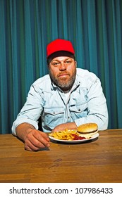 Man With Beard Eating Fast Food Meal. Enjoying French Fries And A Hamburger. Trucker With Red Cap.