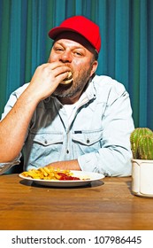 Man With Beard Eating Fast Food Meal. Enjoying French Fries And A Hamburger. Trucker With Red Cap.