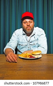 Man With Beard Eating Fast Food Meal. Enjoying French Fries And A Hamburger. Trucker With Red Cap.