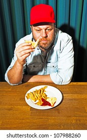 Man With Beard Eating Fast Food Meal. Enjoying French Fries And A Hamburger. Trucker With Red Cap.