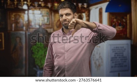 Man with beard giving thumbs down near icon paintings in ornate religious interior building; disapproval judgment.