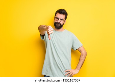 Man With Beard And Green Shirt Showing Thumb Down Sign With Negative Expression