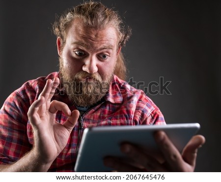 Man with beard and long hair wearing plaid shirt, holding tablet and showing ok sign, satisfied gesture, shoot in studio