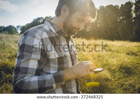 Man with beard looking at his smartphone while sundown Bearded man texting sms on his phone Man using apps for travel or gps navigation help or reading news and texts using 3g and 4g [[stock_photo]] © 