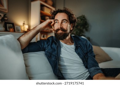 Man with beard and mustache contemplating while sitting comfortably on a sofa at home