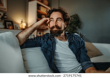 Man with beard and mustache contemplating while sitting comfortably on a sofa at home