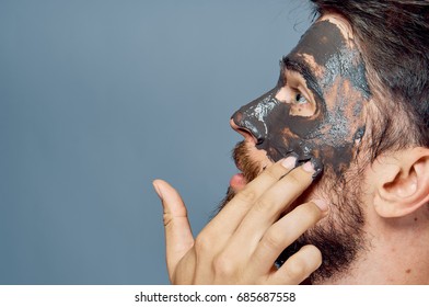 A Man With A Beard On A Black Background Apply Clay Cosmetic Face Mask.