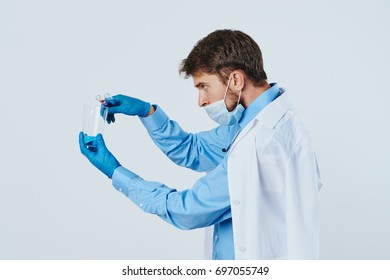 A man with a beard on a light background in a medical dressing gown puts experiments in laboratory vessels, science, scientist.