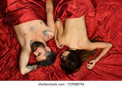 Man with beard and peaceful face lies with pretty lady in bed, top view. Guy and woman with half covered bodies sleep in their bedroom. Love and sex concept. Couple in love on red sheets