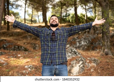Man with beard and plaid shirt of aesthetic lumberjack spreads his arms in the middle of nature with joy