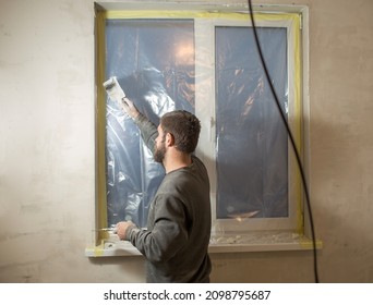 A Man With A Beard Plasters Window Slopes With A Spatula And Putty.

