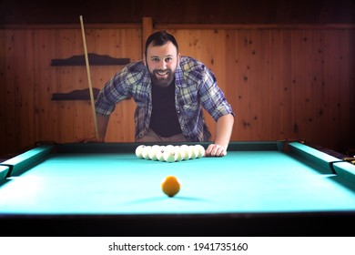 A man with a beard plays a big billiard. Party in 12-foot pool. Billiards in the club game for men. A man with a cue breaks the pyramid. - Shutterstock ID 1941735160