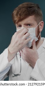 Man With Beard With Serious Face In Laboratory Coat Puts Protective Mask On Isolated On Dark Lab Background