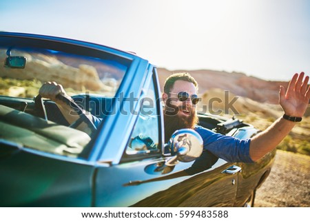 man with beard sitting in vintage car waving