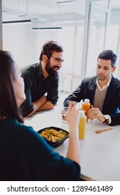 Man With Beard Smiling In The Office Cafeteria While Colleagues Eating