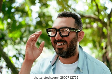Man with a beard smiling and touching spectacles outdoors