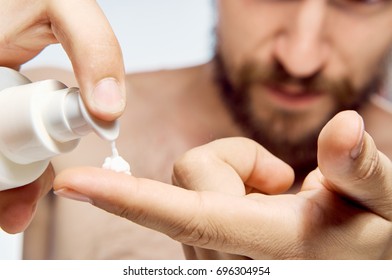 A man with a beard squeezes out skin care cream                               