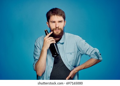 A man with a beard thinks and holds an empty glass bottle on a blue background                               