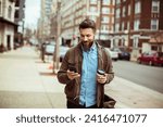 Man with beard using smartphone and holding coffee cup on city street