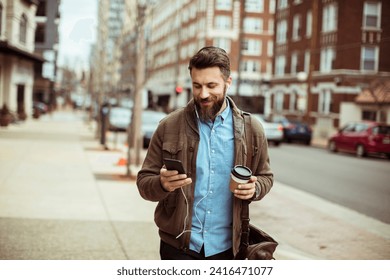 Man with beard using smartphone and holding coffee cup on city street - Powered by Shutterstock