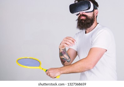 Man With Beard In VR Glasses Beating Pitch, Grey Background. Guy With VR Glasses Play Tennis With Racket. Virtual Sport Concept. Hipster On Busy Face Use Modern Technology For Sport Games.