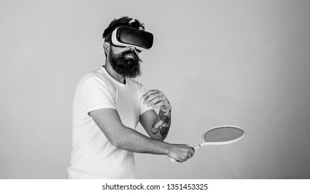 Man With Beard In VR Glasses Beating Pitch, Grey Background. Guy With VR Glasses Play Tennis With Racket. Virtual Sport Concept. Hipster On Busy Face Use Modern Technology For Sport Games.