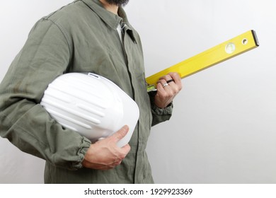 Man With Beard Wearing Worker Uniform Holding Hardhat Under Arm And Level Tool. No Face