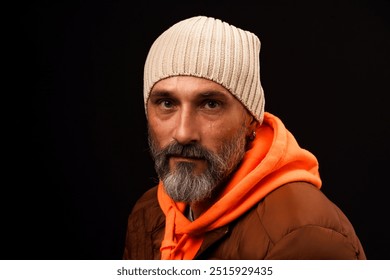 A man with a beard and a white hat is wearing an orange hoodie. He is looking at the camera with a serious expression - Powered by Shutterstock