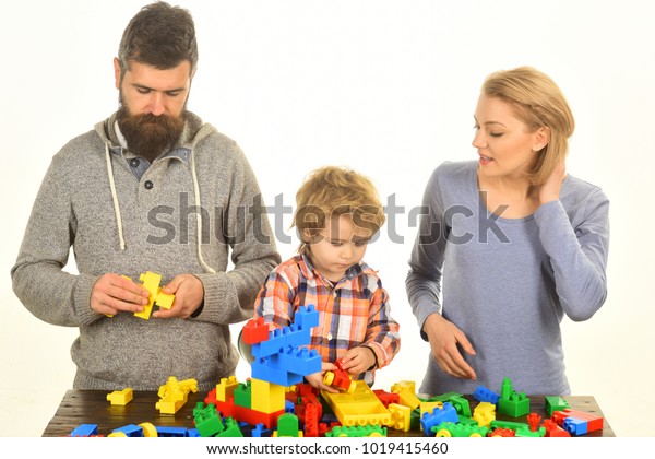Man with beard, woman and boy play on white\
background. Family with busy faces build toy cars out of colored\
construction blocks. Parents and kid in playroom. Kindergarten and\
family concept.