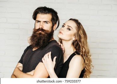 Man With Beard And Woman With Long Blond Hair. Girl And Bearded Hipster. Couple In Love Hug On White Brick Wall. Hipsterism, Subculture, Trend. Fashion, Beauty, Style Concept.