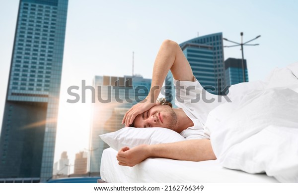 Man in bed and beautiful view of\
cityscape on background. Poor sleep because of urban\
noise