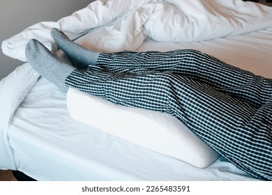a man in bed leans his legs on a leg elevation pillow made of memory foam