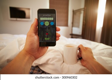 Man In Bed Looking At Health Monitoring App On Mobile Phone