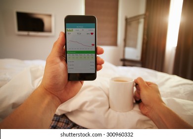 Man In Bed Looking At Health Monitoring App On Mobile Phone