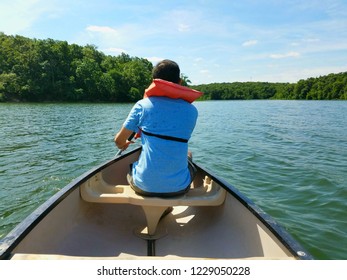 A Man From Behind, With A Lifejacket, Kayaking In A Blue Tshirt In A Green Lake