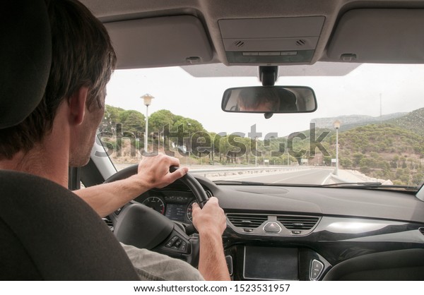 Man\
behind the wheel of a car. Dark interior of the car. Man drives a\
car on the highway among the heels. Man from\
behind.