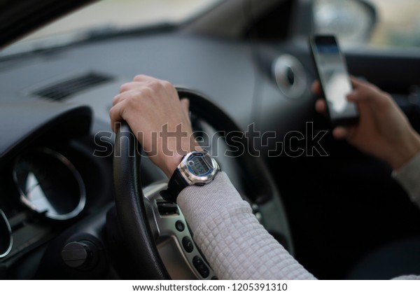 The man behind the wheel writes a message. Hands\
on the wheel.